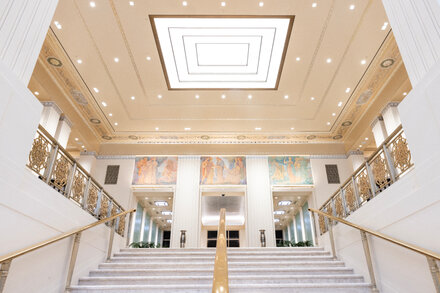 Interior view of the Waldorf Astoria hotel lobby, showcasing its opulent design, high ceilings, and chandelier, with sunlight streaming through large windows.