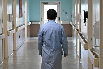 A smiling doctor, dressed in scrubs, standing in a hospital hallway.