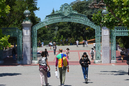 Students at UC Berkeley protest on campus, holding signs and a large banner, reflecting the college's struggle to respond to Trump policies.