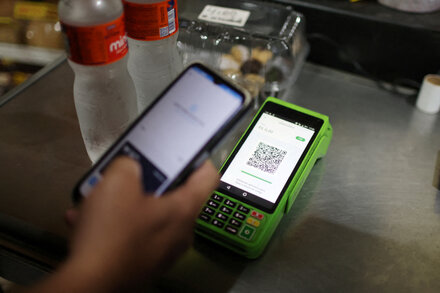 Un teléfono móvil muestra la aplicación de pago digital Pix de Brasil con el logo en el centro y coloridos gráficos alrededor, junto a billetes de reales brasileños y monedas sobre una mesa.