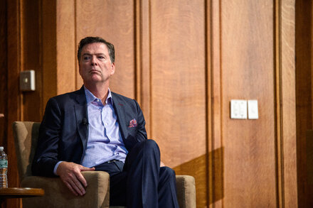 Former FBI Director James Comey in a somber courtroom, facing a judge. Behind him, a packed gallery shows a mix of shock and confusion among journalists and onlookers. The image captures the tension and gravity of the moment.