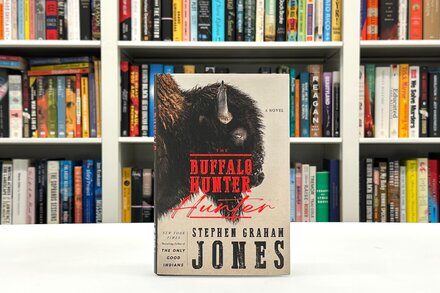 A close-up of the book cover for 'The Buffalo Hunter Hunter' by Stephen Graham Jones. The cover features a stark, dark landscape with a lone, silhouetted figure holding what appears to be a spear or rifle, set against a muted sky.