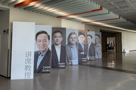 A group of young, diverse professionals in a modern office setting, some looking at a screen, others discussing. The setting appears to be a tech or research company in China.