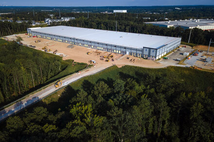 A large, modern data center facility with multiple rows of server racks, some illuminated with blue lights, suggesting high technology and energy consumption. The setting is clean and industrial, possibly with a hint of an outdoor or natural element in the background, subtly alluding to environmental impact or potential for green energy.