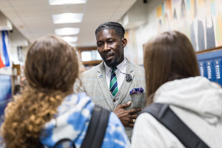 Des Moines Schools Superintendent Dr. Lisa Williams, a woman in a business suit, looking serious and professional, stands in front of a blurred school backdrop.