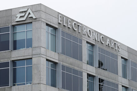 A video game controller with the Electronic Arts logo on it, superimposed over a blurred background of a modern office building or data center, symbolizing the company's significant presence and recent major acquisition.