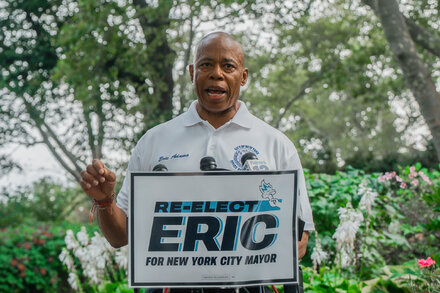 New York City Mayor Eric Adams at a press conference, looking serious, with city hall in the background.