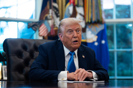 Donald Trump speaking at a rally, with a crowd of supporters behind him, addressing topics like a government shutdown and urban planning.