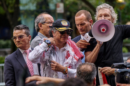 El presidente colombiano Gustavo Petro habla en un podio con un fondo de bandera colombiana, mirando hacia la derecha.