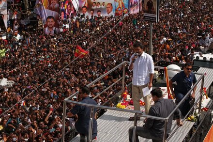 A large crowd of people gathered at an outdoor political rally in India, with some individuals looking distressed. Police officers are visible in the foreground, trying to manage the situation.