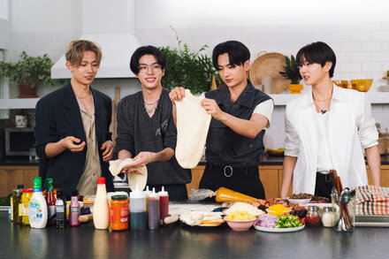 K-pop group Enhypen members smiling while holding slices of pizza, one with corn toppings