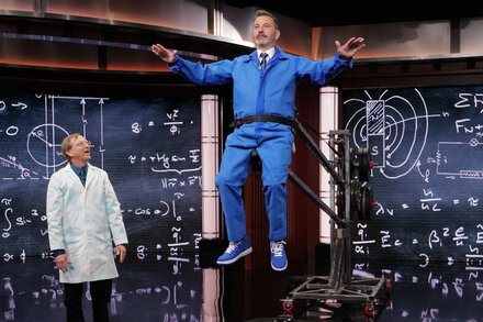 Jimmy Kimmel standing at a microphone on a stage, with a serious expression, in front of an audience.