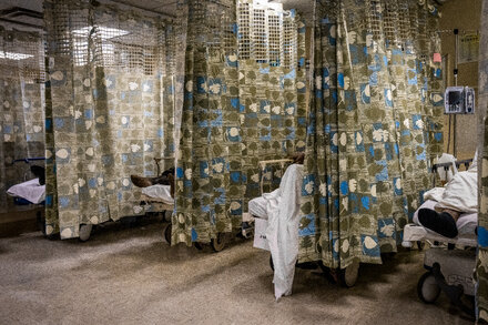 A diverse group of doctors in scrubs and white coats stand together, some holding stethoscopes, looking concerned. The background is a blurred hospital corridor or medical office. The image illustrates the issue of visa fees affecting foreign doctors.