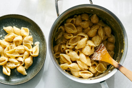 A close-up of a bowl of minimalist pasta, generously tossed with roasted garlic, fresh herbs, and a light sauce. The pasta is perfectly al dente, with whole roasted garlic cloves visible.