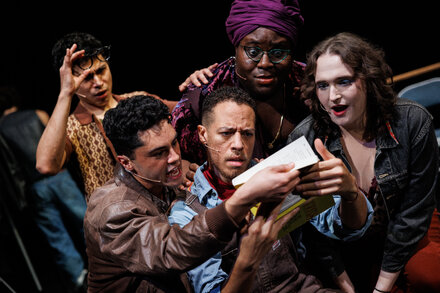 A modern reinterpretation of Mozart's 'The Marriage of Figaro' set on Fire Island. The image shows actors in contemporary clothing, possibly at a beach house or outdoor party, with vibrant colors and a dramatic pose.