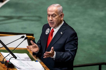 Israeli Prime Minister Benjamin Netanyahu holds up a large card with a QR code during a speech. The QR code is prominently displayed against a backdrop of the UN logo.