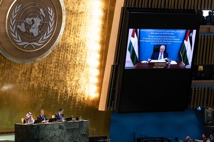 Palestinian Authority leader Mahmoud Abbas speaking at a podium, with a Palestinian flag visible.