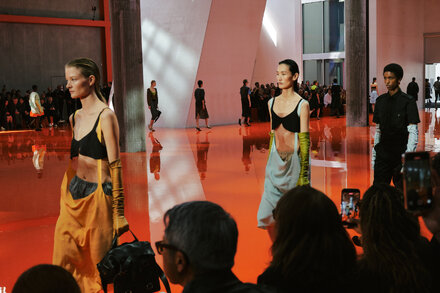 A model in a high-fashion, protective-looking outfit from Prada's collection, suitable for a futuristic or apocalyptic scenario, against a minimalist backdrop.