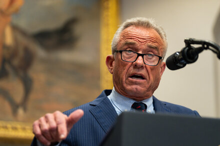 Robert F. Kennedy Jr. at a UN event, speaking at a podium with the UN logo behind him, representing the U.S. rejection of global health goals.