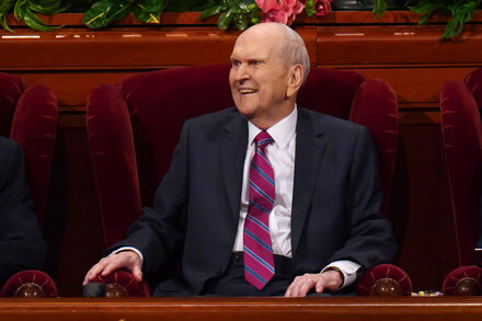 Russell M. Nelson smiling and looking forward, wearing a suit and tie, against a blurred background.