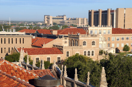 Two people, possibly students, walk past a building on the Texas Tech University campus. The building is a typical university brick building with large windows.