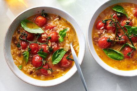 Close-up of a bowl of vibrant red tomato soup, garnished with fresh basil leaves, suggesting a rich and flavorful dish.