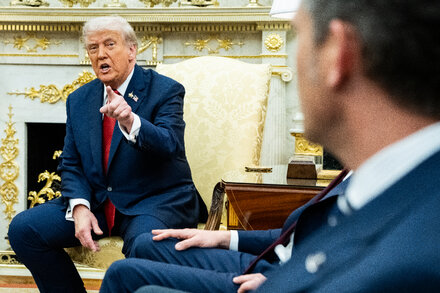 Donald Trump speaking at a podium, with a focused expression, in front of a backdrop. The image likely depicts him discussing economic policies or trade.