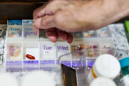 Tablets and capsules of various medicines arranged on a surface, with a blurred background suggesting a pharmacy or factory, illustrating the potential impact of tariffs on drug prices.