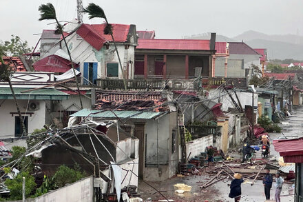 A submerged street in a Vietnamese town, with palm trees bent by strong winds and debris floating in floodwaters, following Typhoon Bualoi.