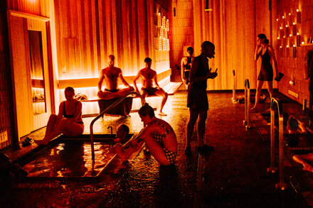 Two people in an ancient bathhouse looking relaxed and connected, with steam rising around them.