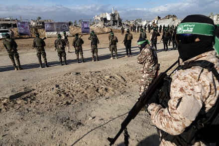 Palestinian militants in Gaza Strip, possibly members of Hamas, standing in formation. The image suggests a military presence and ongoing conflict. Focus is on uniformed individuals and weaponry, with a backdrop of urban destruction or a training ground. This relates to discussions about Hamas disarming.