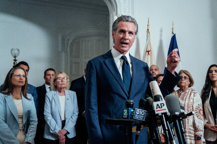 California Governor signing an AI law at a desk with advisors present, with the state seal visible in the background.