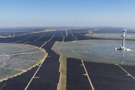 An expansive aerial view of a massive solar panel farm stretching across a flat, high-altitude landscape under a clear sky.