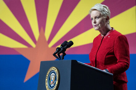 Cindy McCain smiling and looking forward, with a blurred background. She is wearing a professional suit jacket.