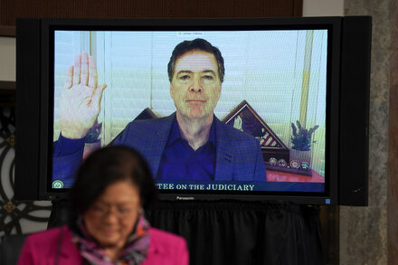 Former FBI Director James Comey in a courtroom, looking serious, during an arraignment hearing. The background suggests a formal legal setting.