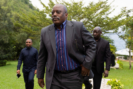 Former Congolese President Joseph Kabila standing with a serious expression, wearing a suit and tie, against a blurred background.