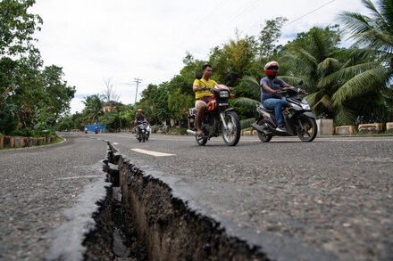 Rescue workers search through rubble after a deadly earthquake in the Philippines. Buildings are damaged, and debris is scattered.