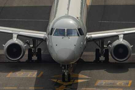 Aviones en una pista de aeropuerto con una torre de control de tráfico aéreo al fondo, y el cielo parcialmente nublado. La imagen sugiere retrasos o interrupciones en los viajes aéreos.