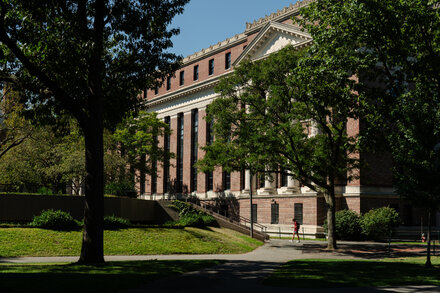 Harvard University building exterior, possibly a library or administrative office, with the Harvard Crimson logo subtly incorporated or in the foreground.