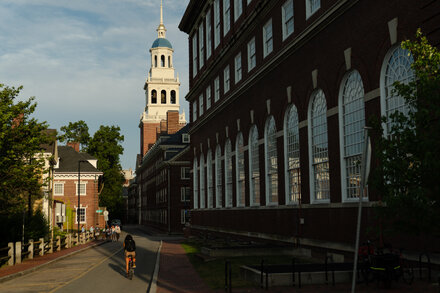 Massachusetts Hall at Harvard University, an iconic building, is shown on a sunny day with students walking nearby.