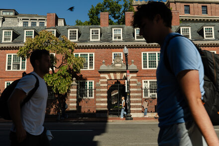Students studying in a busy Harvard University library, with books scattered on tables and laptops open.
