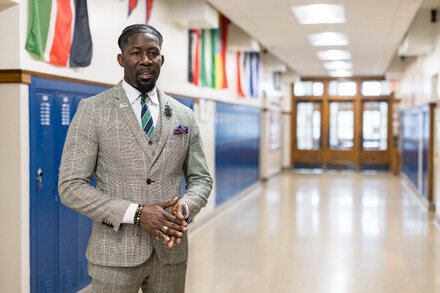 A man in a suit, likely a schools superintendent, stands in front of a school building or public facility, with a serious or reflective expression. The image should convey professionalism and perhaps the weight of recent events.