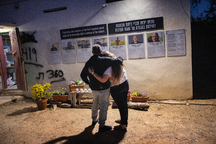 A group of people, possibly family members of hostages, holding up signs with faces and names, pleading for their release.
