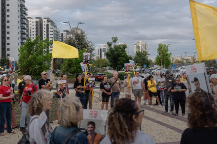 A group of people, possibly family members of hostages, holding signs and photos, some with distressed expressions, at what appears to be a public gathering or protest.