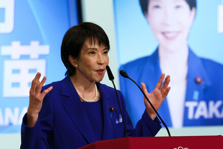 Sanae Takaichi, a prominent Japanese politician, smiles at a podium. She is the leading candidate to become Japan's first female prime minister.