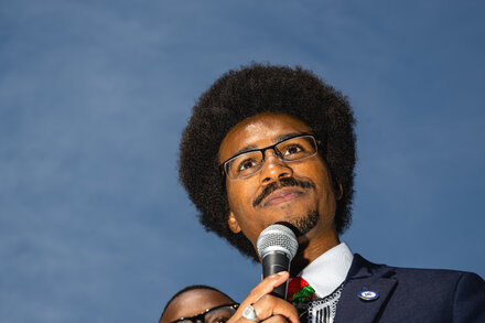 Justin Pearson, Tennessee Democrat and state representative, stands confidently with his hands clasped in front of him, looking directly at the camera. He is wearing a suit jacket over a collared shirt. The background is slightly blurred.