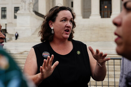 Katie Porter looking serious and engaged during a television interview, with a microphone visible, discussing the California Governor's race.