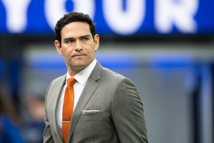 Former NFL quarterback Mark Sanchez in a hospital bed, looking concerned, with medical equipment visible. He has an arm bandaged.