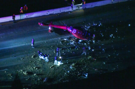 Debris of a crashed medical helicopter scattered across a highway, with emergency vehicles and personnel visible in the background, signaling a recent accident in Sacramento.