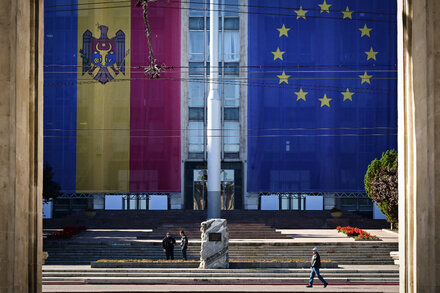 A woman walks past a large, colorful mural depicting a map of Moldova with a European Union flag next to it, and a Russian flag on the other side. The mural suggests the country's geopolitical struggle.